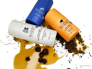 A blue bottle of night time moisturiser, an orange bottle of day time moisturiser, a grey bottle of gentle cleanser, next to natural plant ingredients